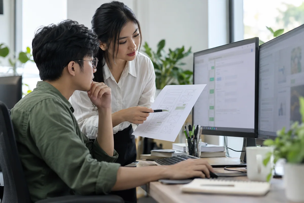 Illustrative software developers reviewing paper wireframes at a workstation